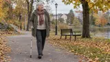 Äldre kvinna som går med en justerbar käpp i aluminium längs en parkväg på hösten
