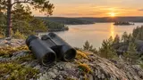 Kompakt kikare på en mossig klippa med utsikt över en svensk sjö och tallskog