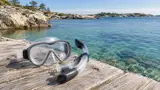 Snorkelmask med snorkel på en brygga ovanför klart vatten i skärgården